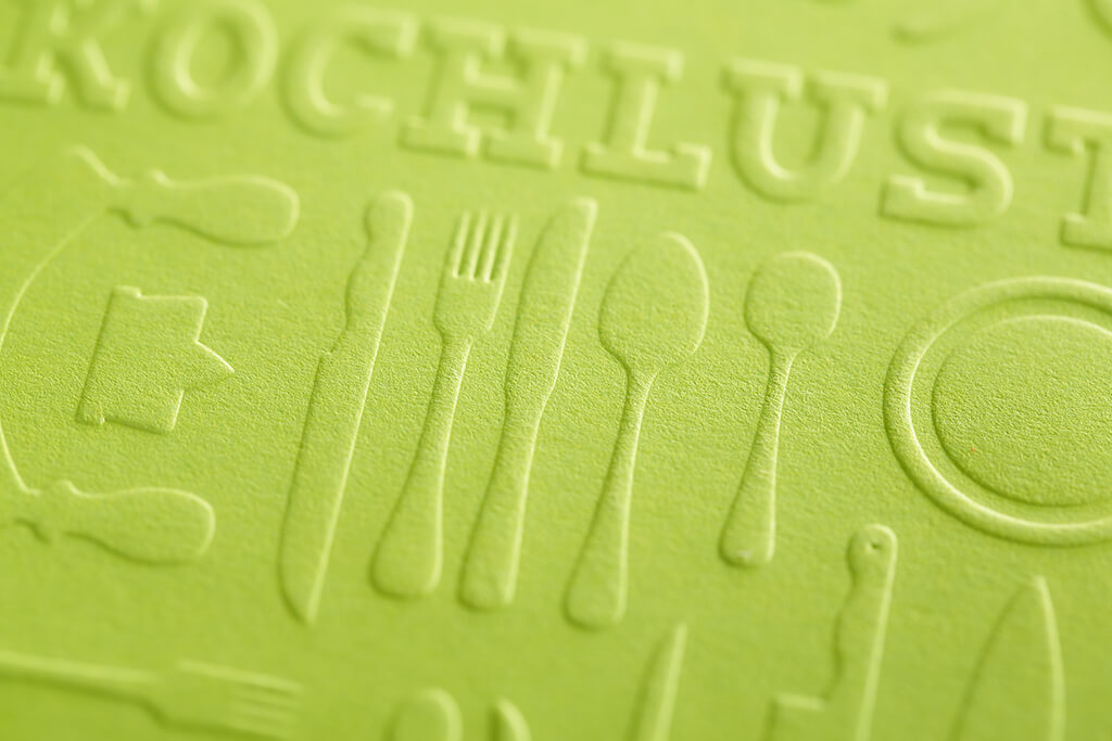 Detailaufnahme einer hellgrünen, geprägten Einlage für das Kochbuch „Kochlust“ mit verschiedenen Besteck-Symbolen und haptischer Oberflächenstruktur.