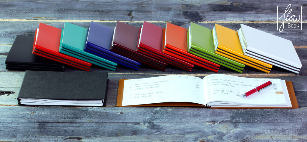 Eine Auswahl bunter Flow-Book Notizbücher in verschiedenen Farben auf einem Holztisch, um effizient persönliche Ziele zu erreichen.