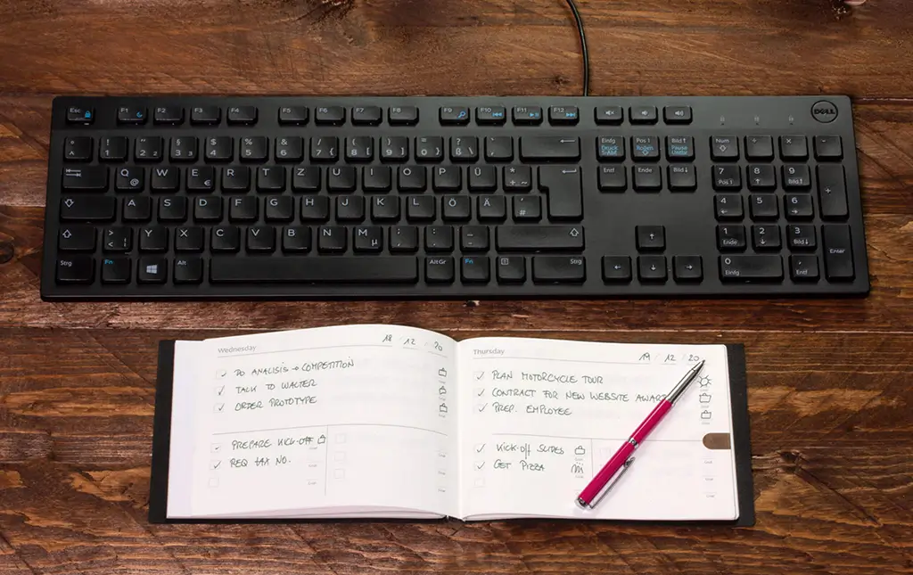 X17 A5+ Quer Terminplaner mit handschriftlicher To-do-Liste neben einer schwarzen Computertastatur auf einem Schreibtisch aus Echtholz.