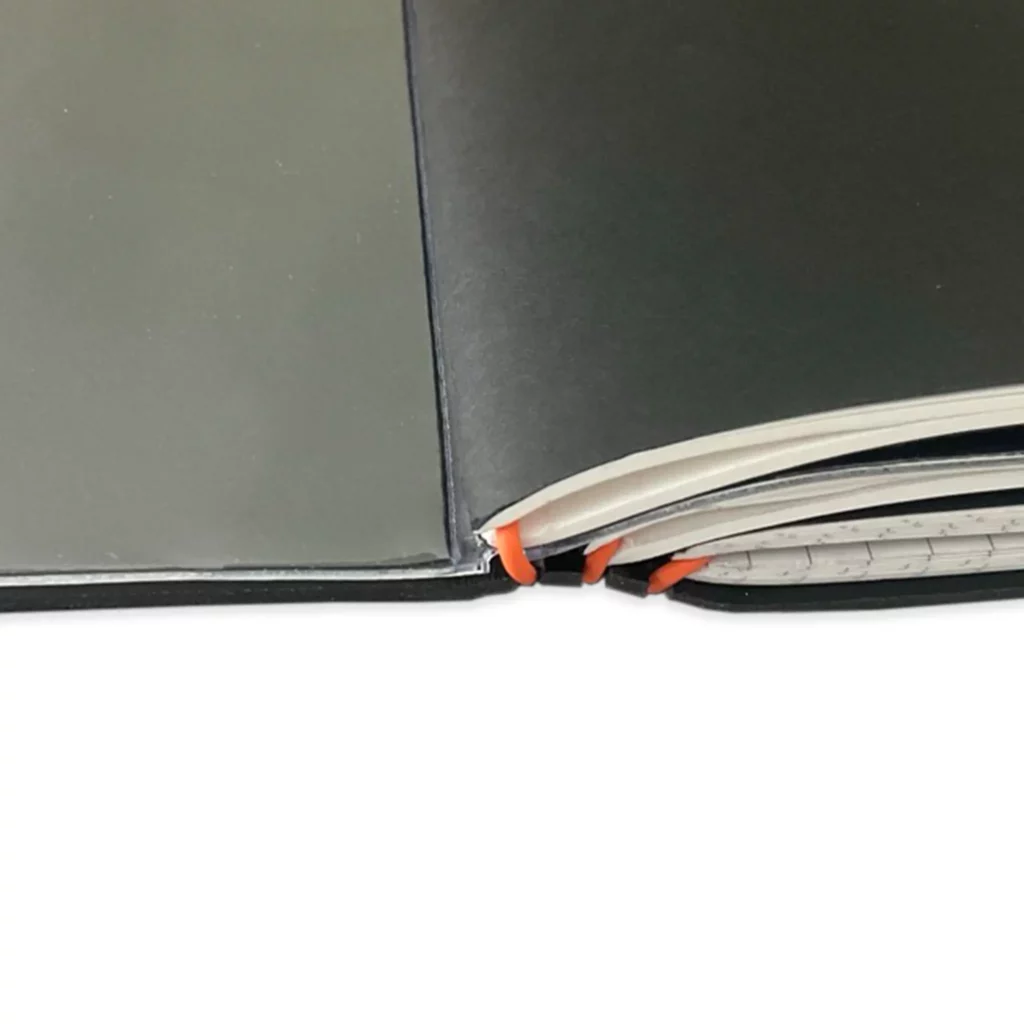 Nahaufnahme des X17 Book-by-Book Systems: Detailansicht der schwarzen Lederhülle mit orangefarbenen ElastiX, die mehrere Hefteinlagen sicher fixieren.