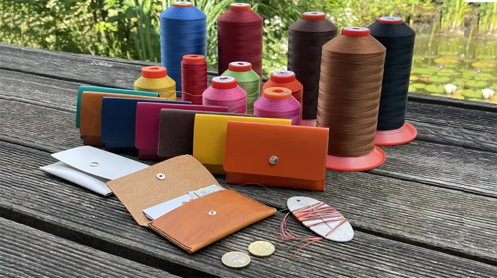 Bunte Leder-Geldbörsen und Garnrollen auf einem Holztisch im Freien – Projekt: Do-it-yourself Börse Leder mit Nadel und Faden.